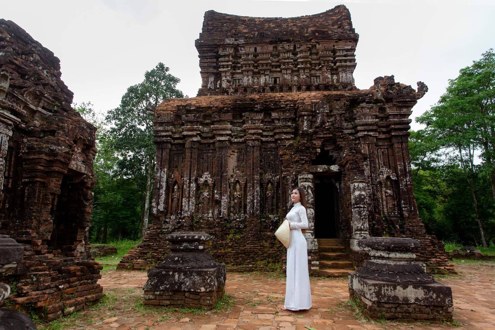 Woman standing before a red-brick Cham temple tower at My Son Sanctuary