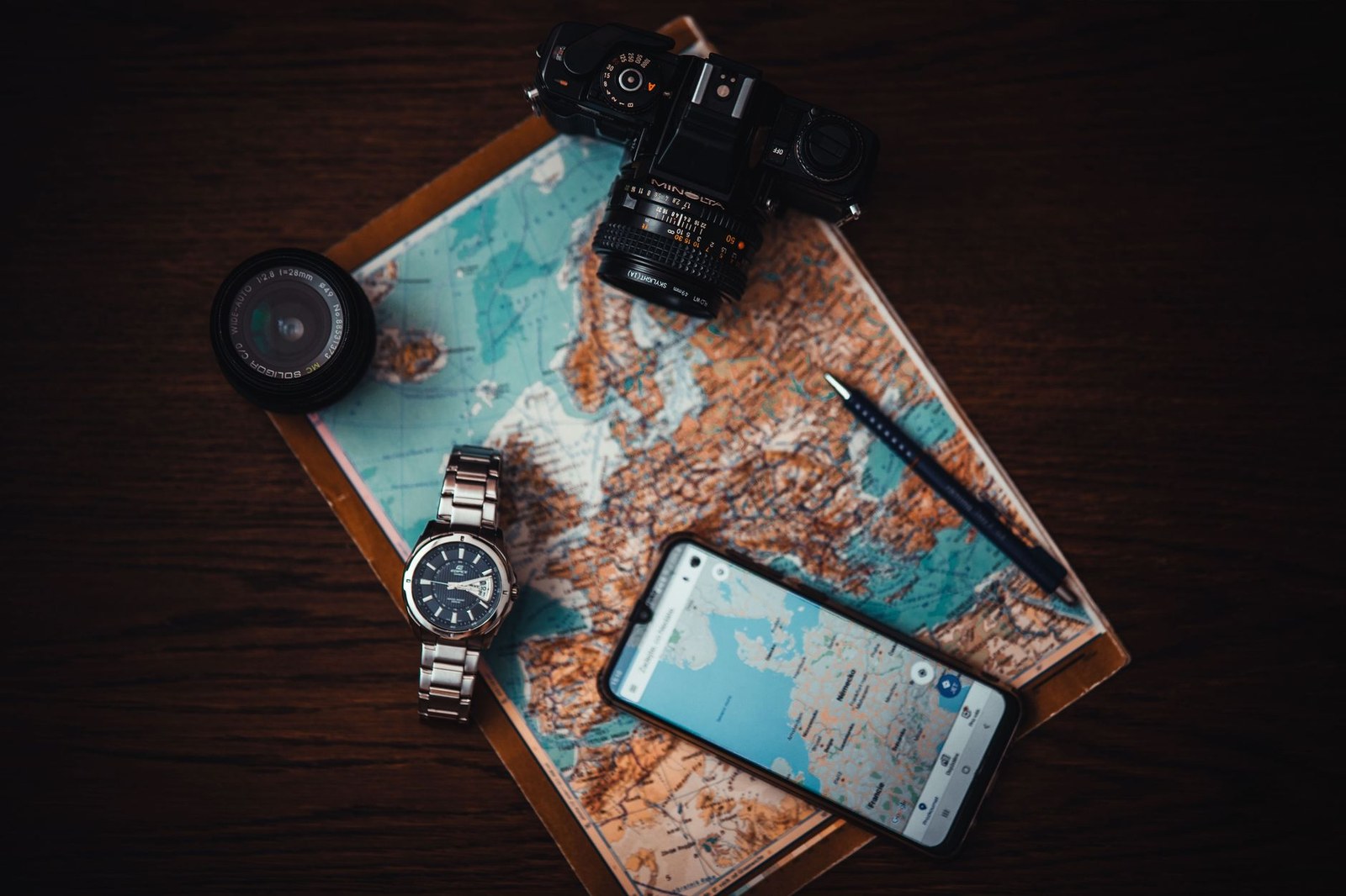 Flat lay of a paper map, film camera, watch and smartphone showing a navigation app