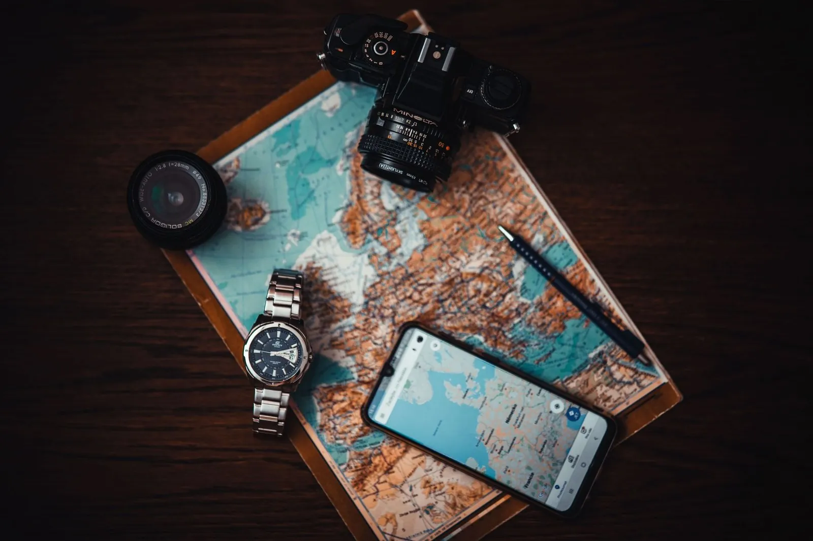 Flat lay of a paper map, film camera, watch and smartphone showing a navigation app