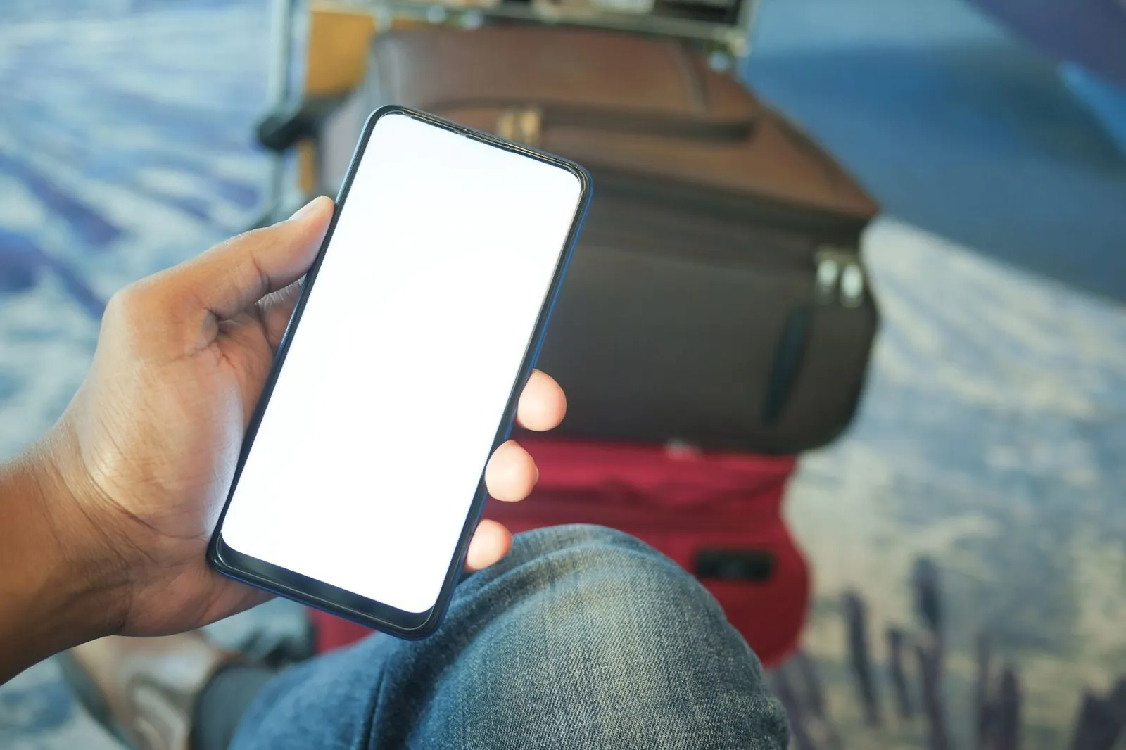 Traveler holding a smartphone beside a suitcase at an airport terminal