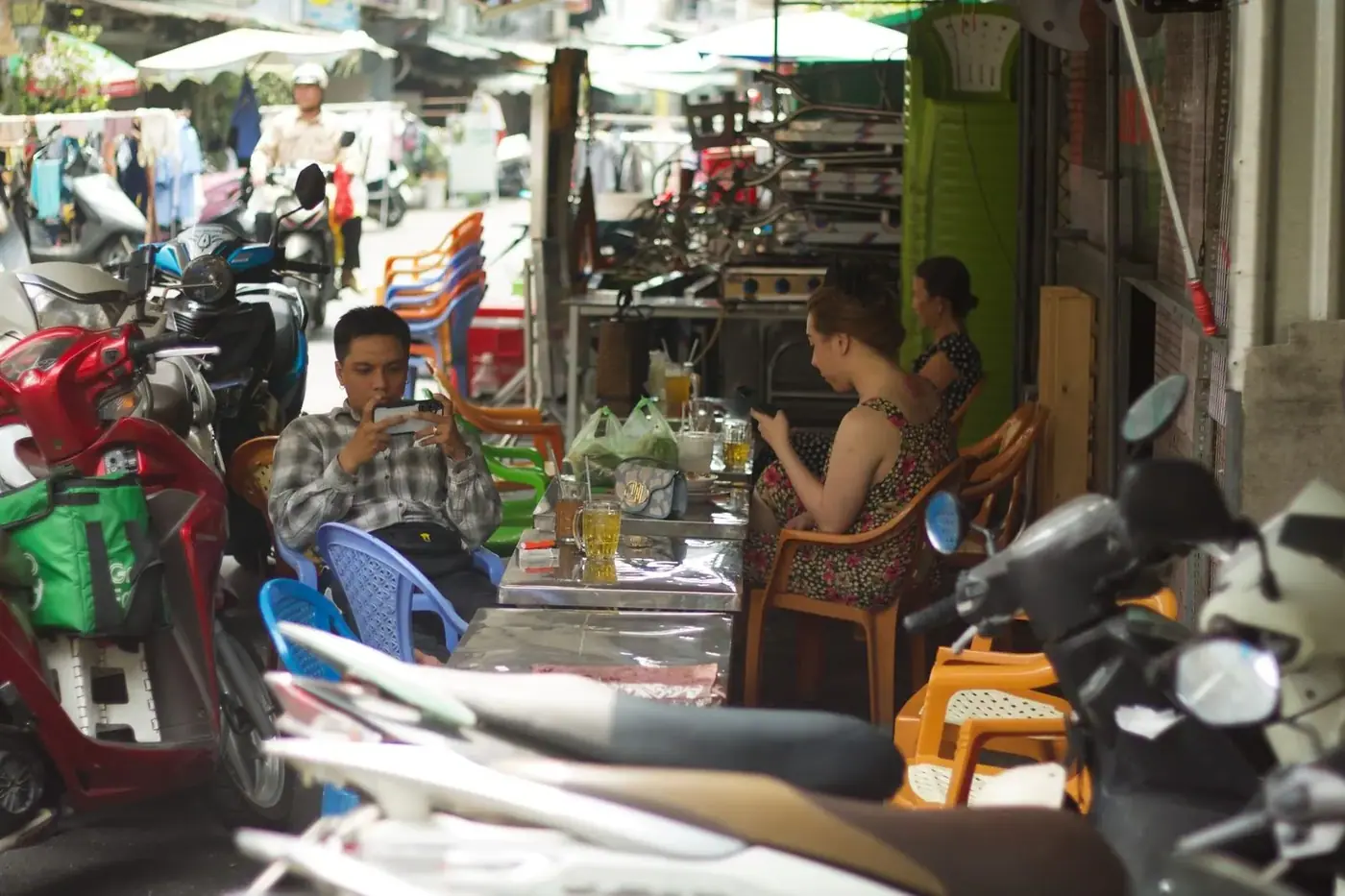 People using smartphones at an outdoor street cafe among parked scooters in Vietnam