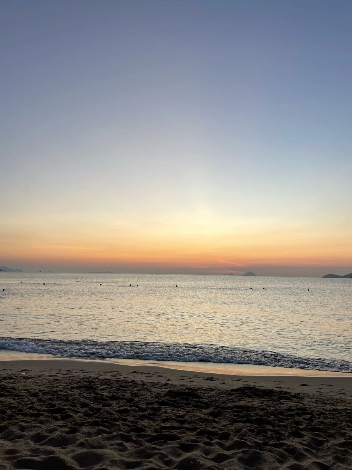 Sunrise over calm sea with swimmers and small islands on the horizon from a sandy beach
