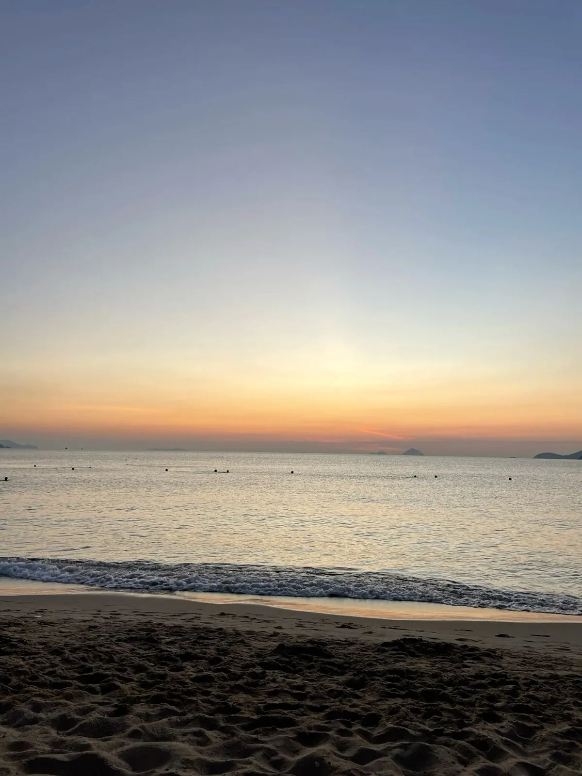 Sunrise over calm sea with swimmers and small islands on the horizon from a sandy beach