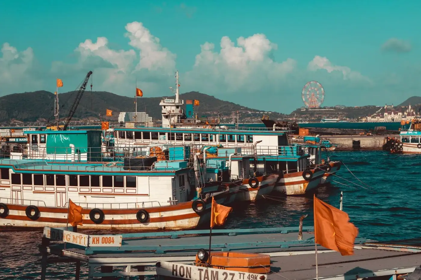 Wooden passenger ferries with Vietnamese flags moored in a harbor with hills behind
