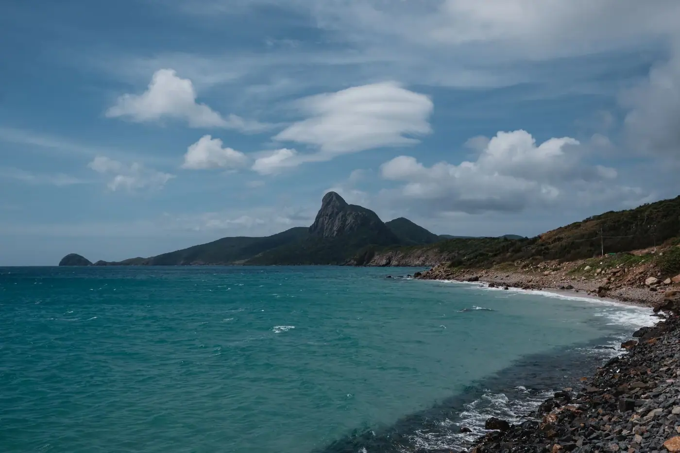 Rocky coastline and mountain peak on Con Dao island under a bright sky