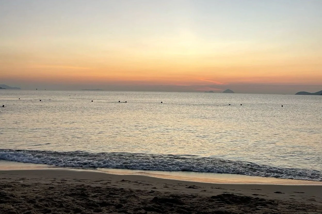 Calm shallow sea with a thin wave line on dark sand just after sunset