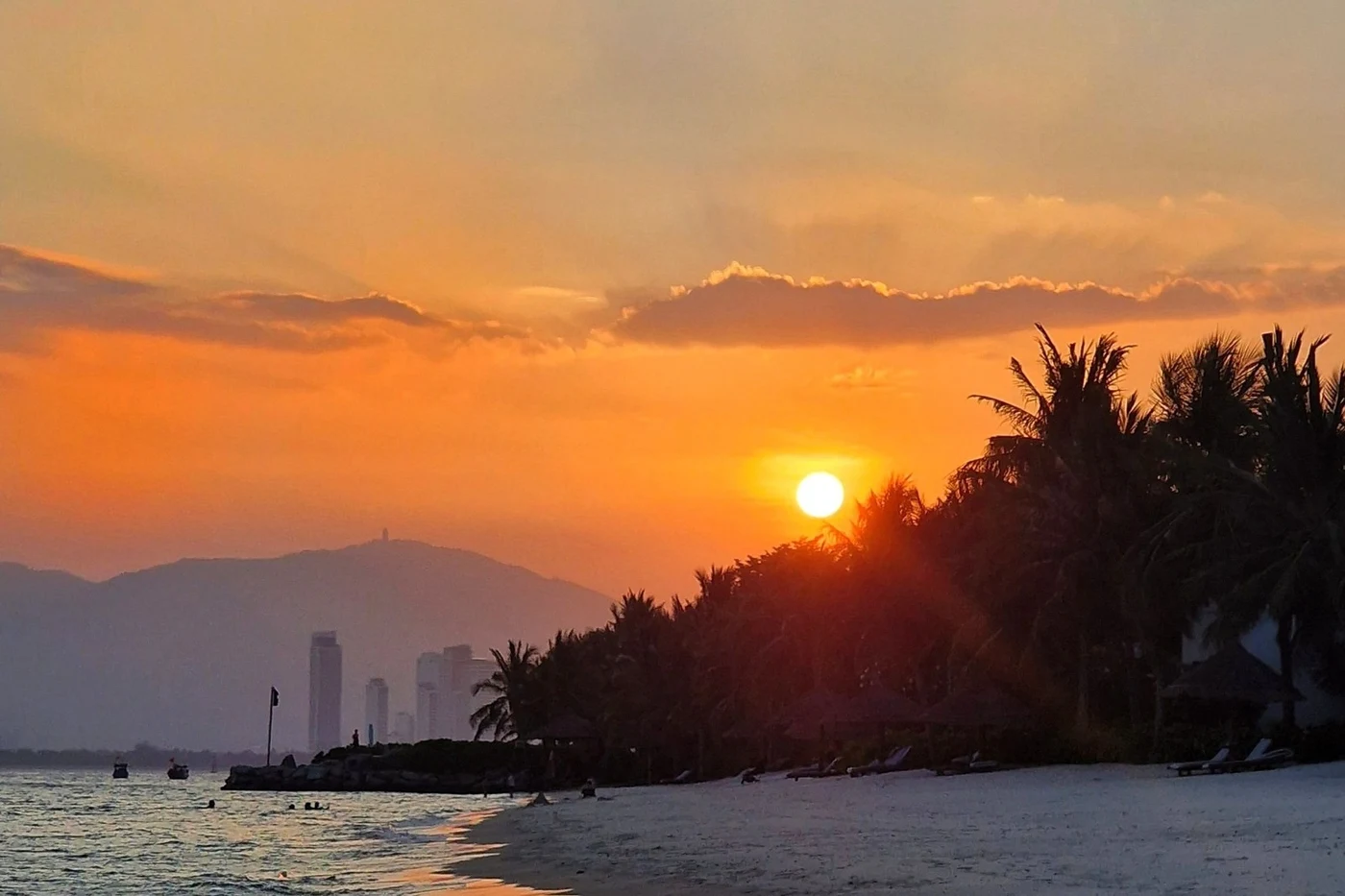 Sun setting over a palm-lined shore with the Nha Trang skyline in the distance