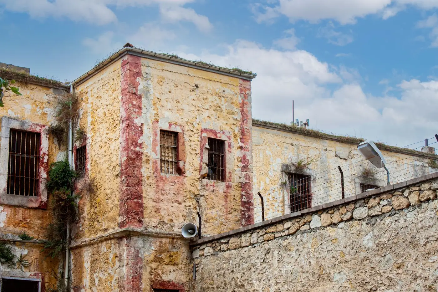Weathered colonial prison block with barred cell windows under blue sky