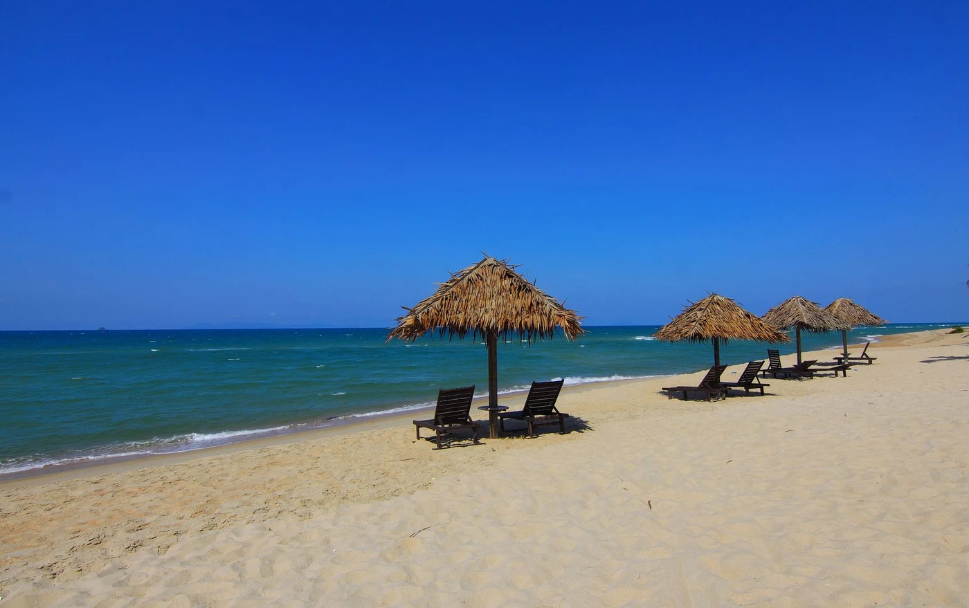 Empty beach with thatched umbrellas and loungers facing a calm turquoise sea