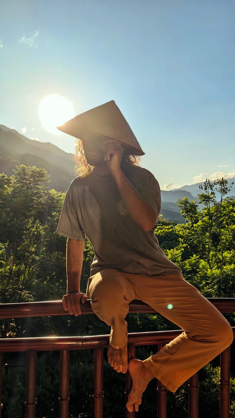 Traveler in a conical hat silhouetted against sunset on an eco-lodge terrace