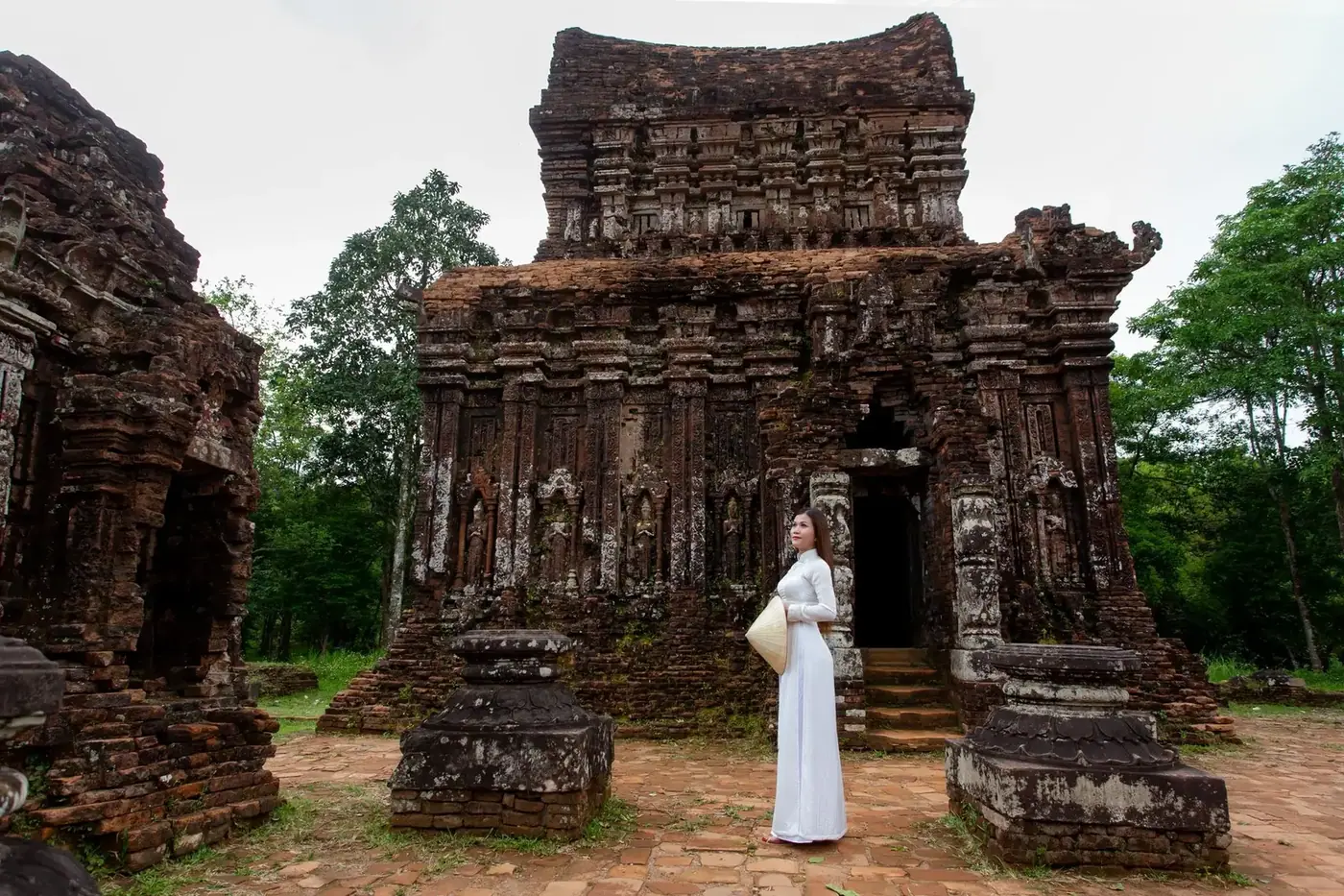A visitor in white ao dai stands before ancient brick Cham towers at My Son Sanctuary