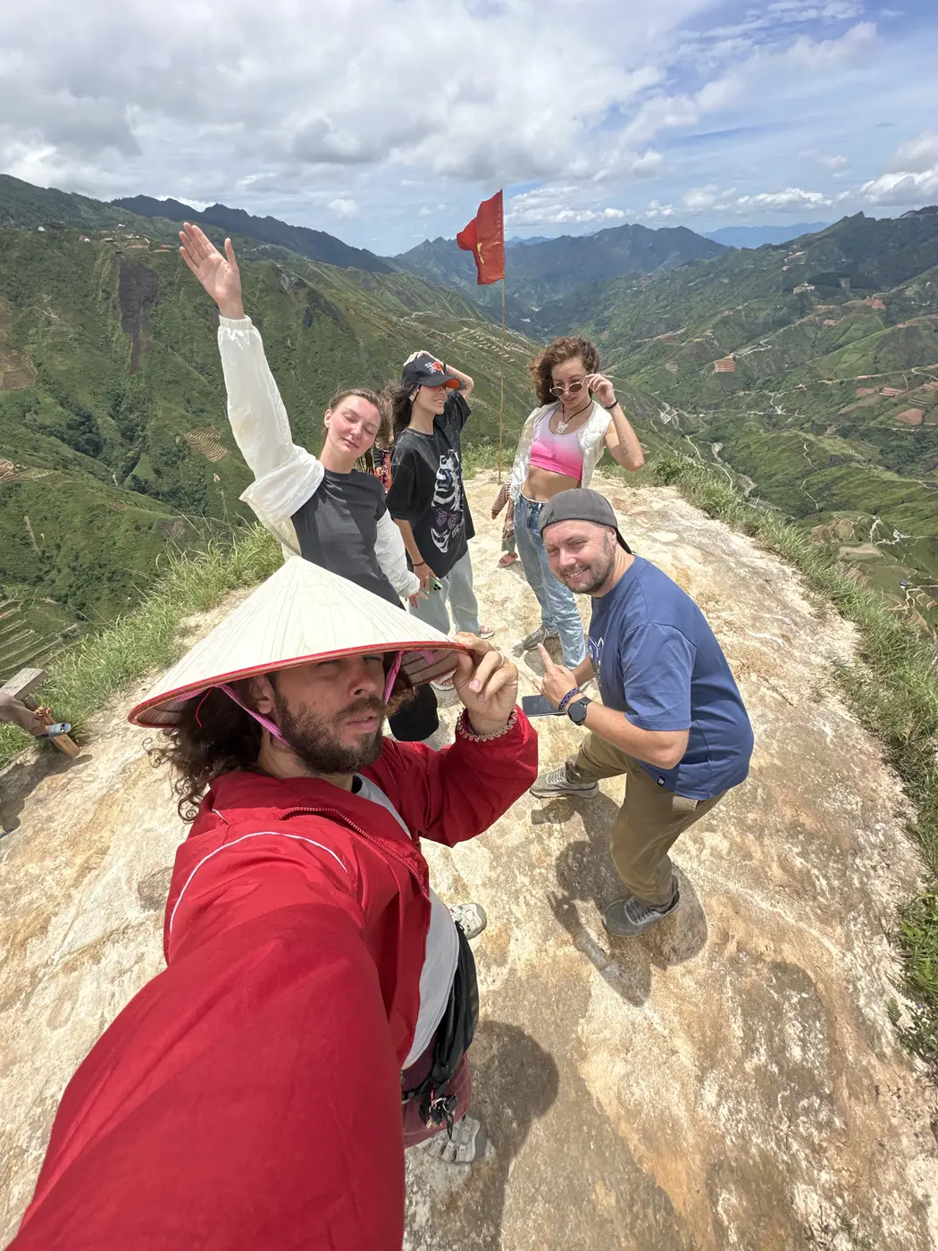 Group selfie at a Ha Giang mountain summit with a Vietnamese flag
