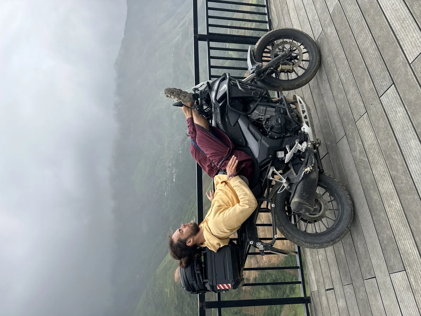 Rider resting on a motorbike at a wooden viewpoint over Ha Giang valley