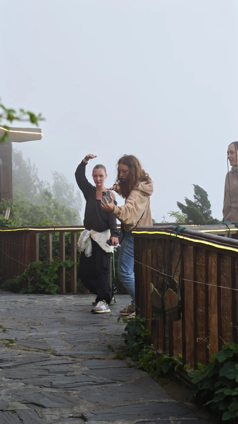 Two travelers take a selfie on a wooden terrace in the fog