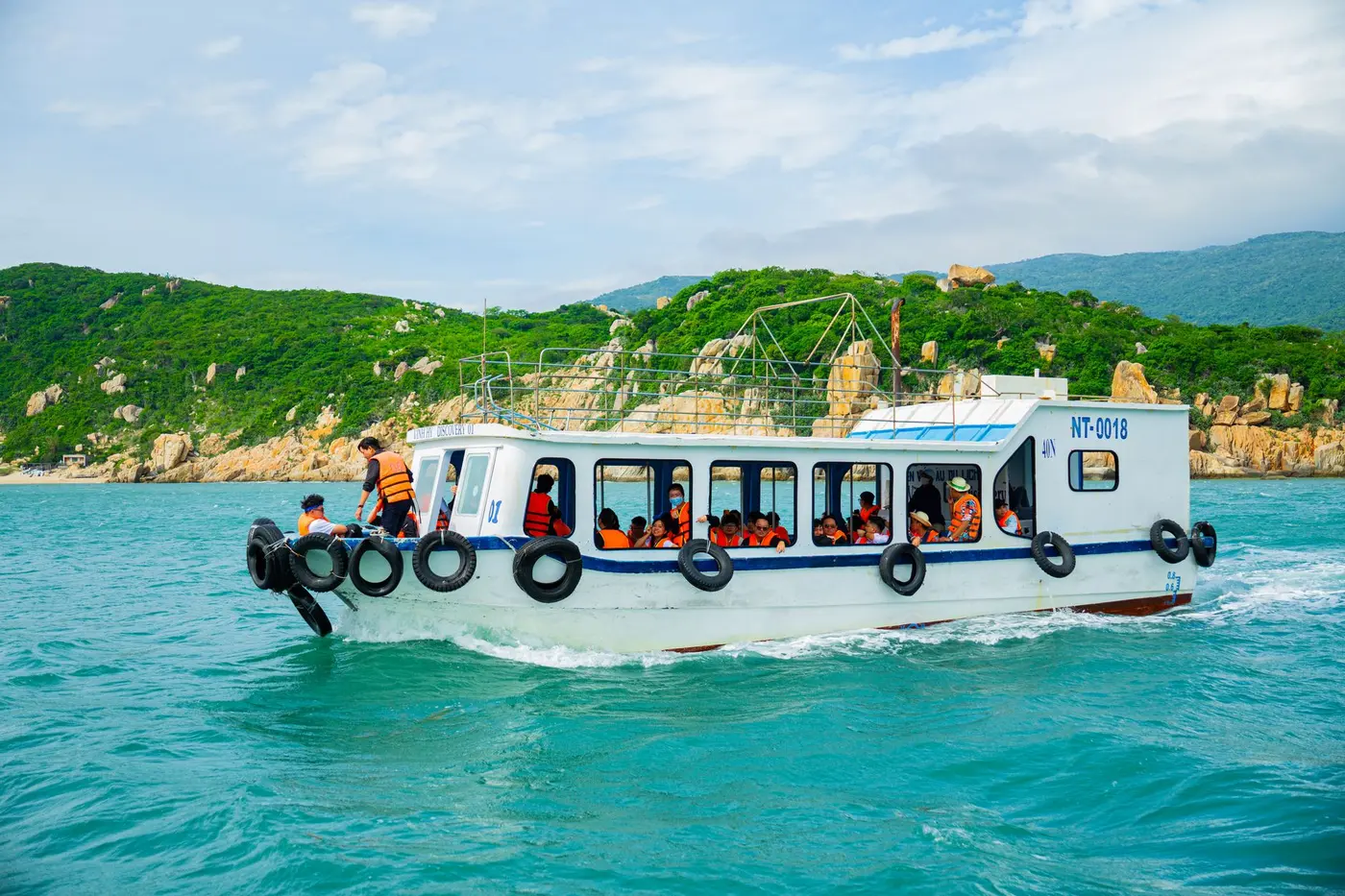 A boat carrying tourists in life jackets along a lush green coastline.