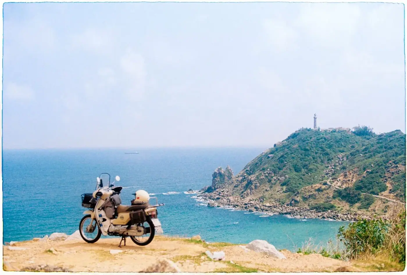 Motorbike parked on a coastal cliff overlook with a lighthouse headland in the distance
