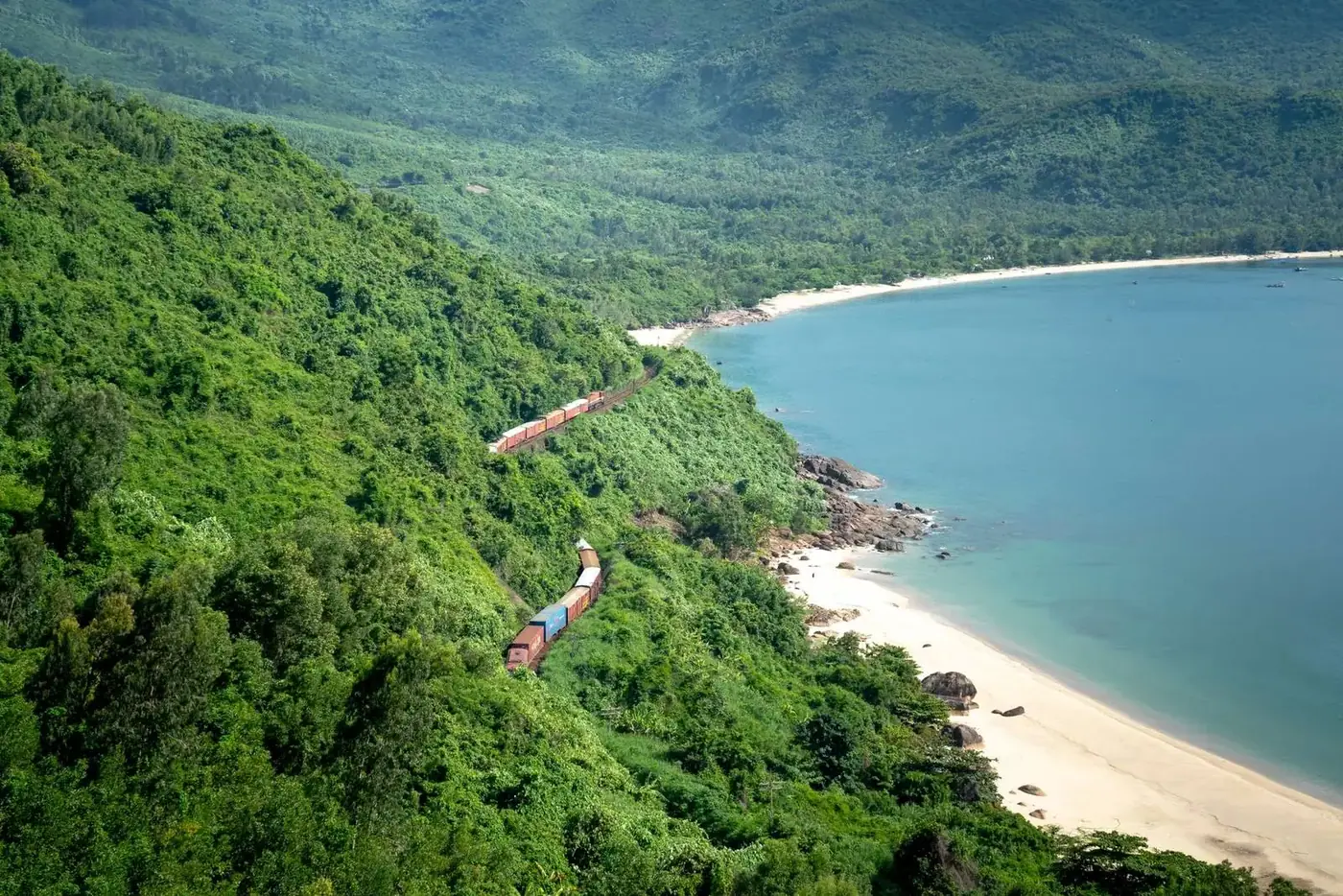 Reunification Express train tracks cut into green mountains above a white-sand beach