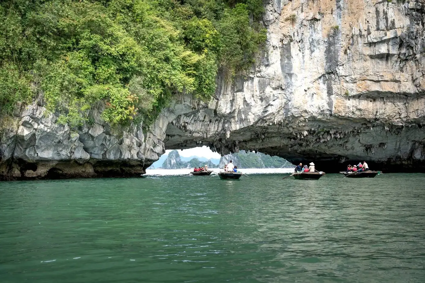 Small rowboats carrying day-trip visitors under a limestone cave arch
