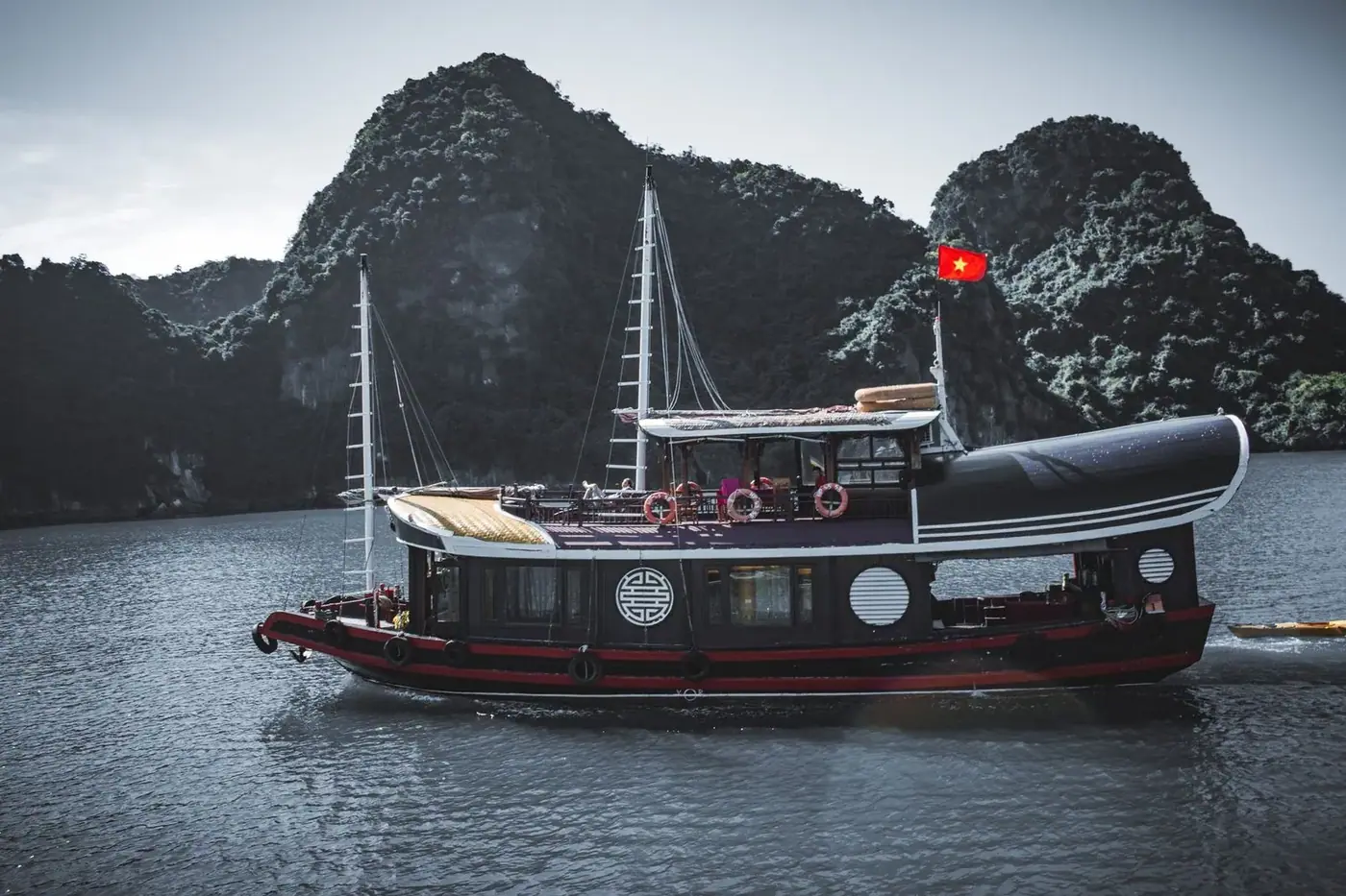 Traditional junk boat sailing past Ha Long Bay’s karst cliffs