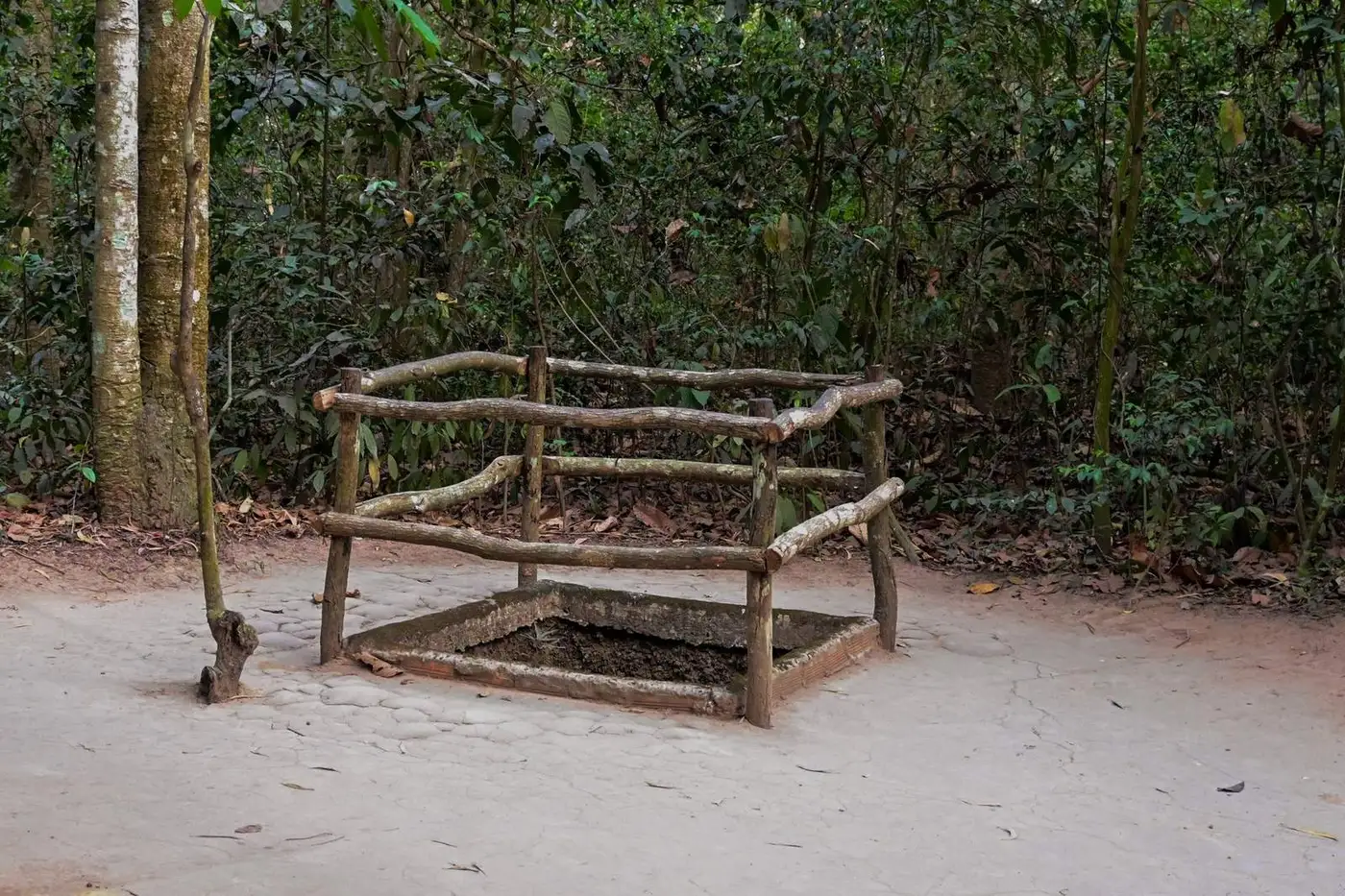Wooden railing around a tunnel hatch in the forest at the Cu Chi tunnels