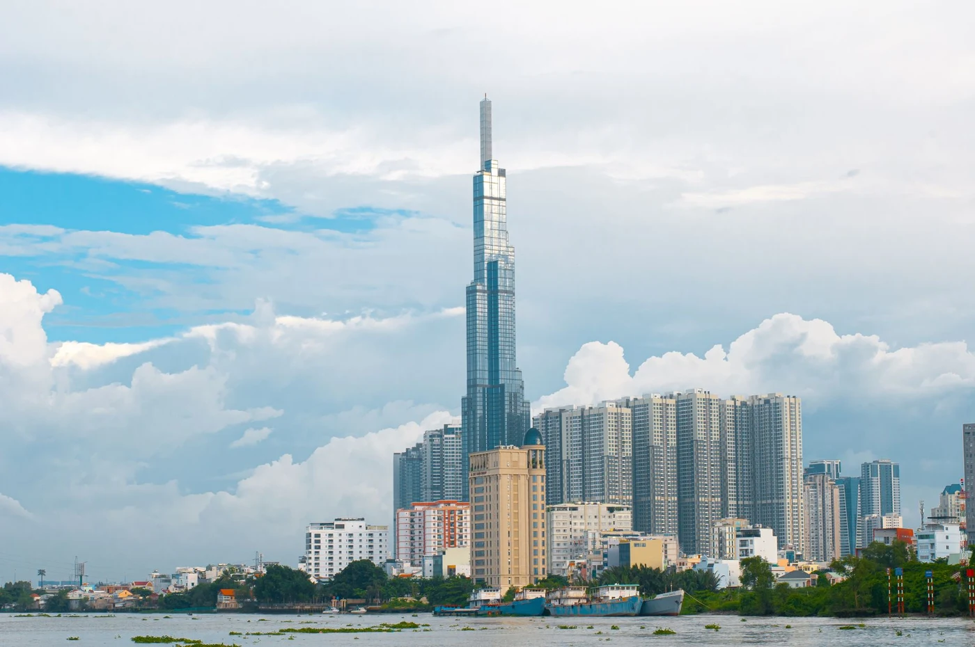 Landmark 81 tower and Saigon River under a bright sky with white clouds