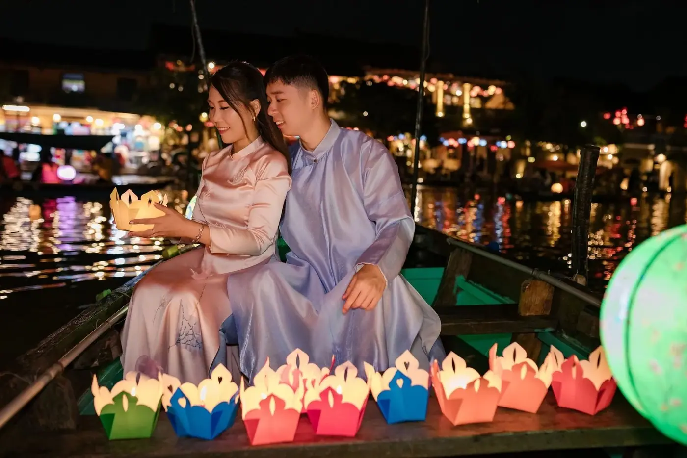 Couple holding a lit paper lantern on a boat at night