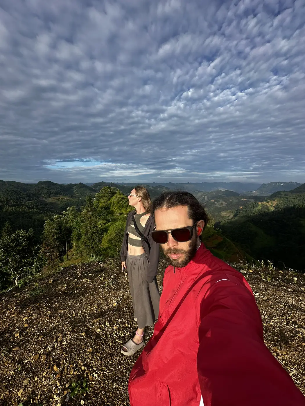 Couple standing on a ridge overlooking a wide backlit mountain valley