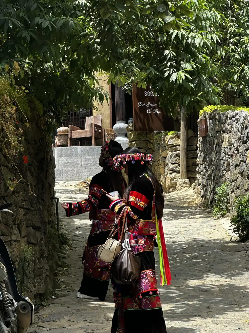 Two Hmong women in embroidered traditional dress walking a stone mountain lane