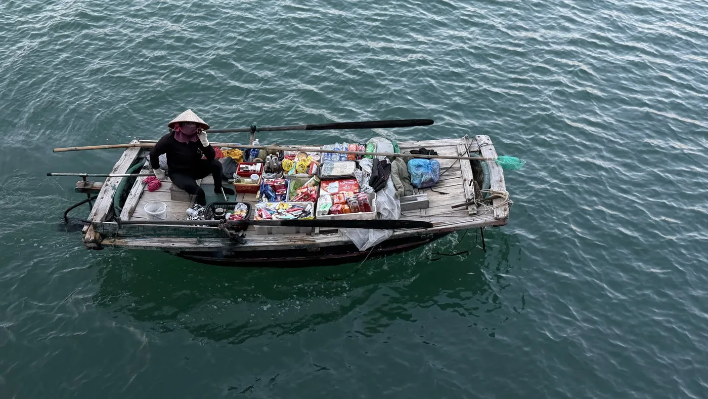 Boat vendor with snacks and drinks seen from above on the green water of Ha Long Bay