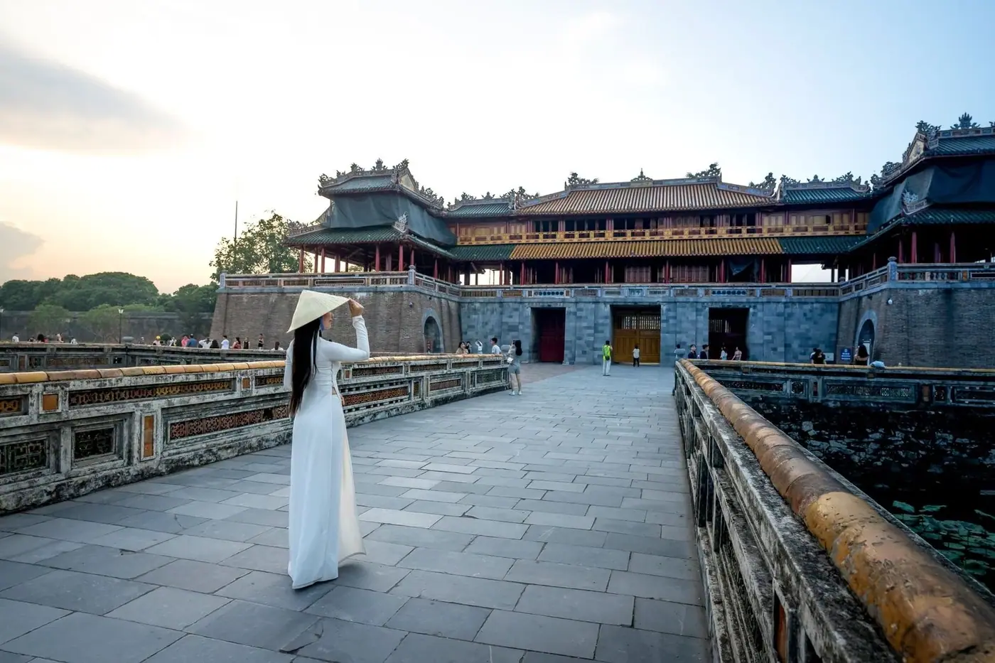 Woman in ao dai crossing the moat bridge to Hue Imperial City gate