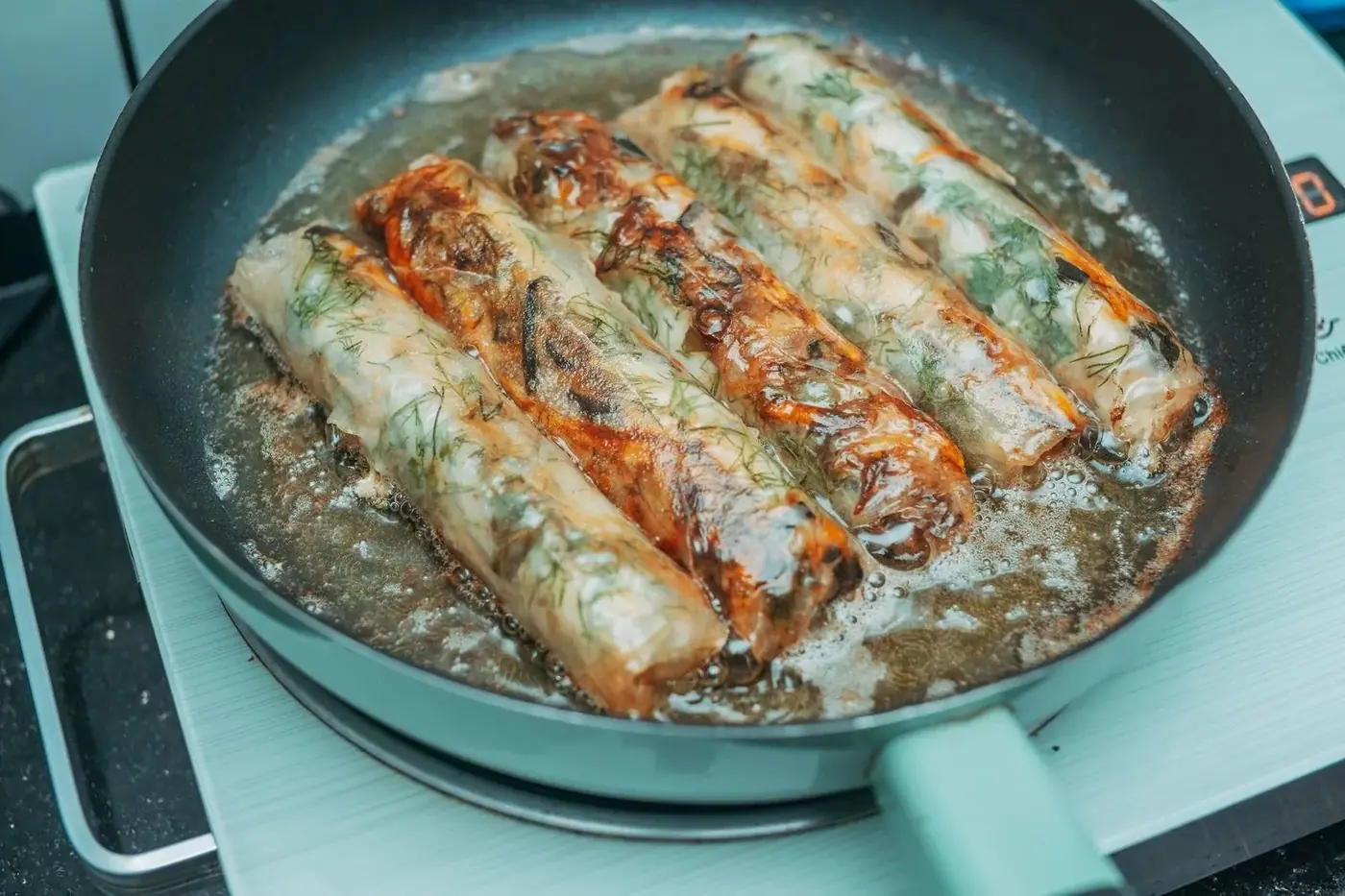 Crispy fried spring rolls sizzling in a wok at a Hoi An cooking class