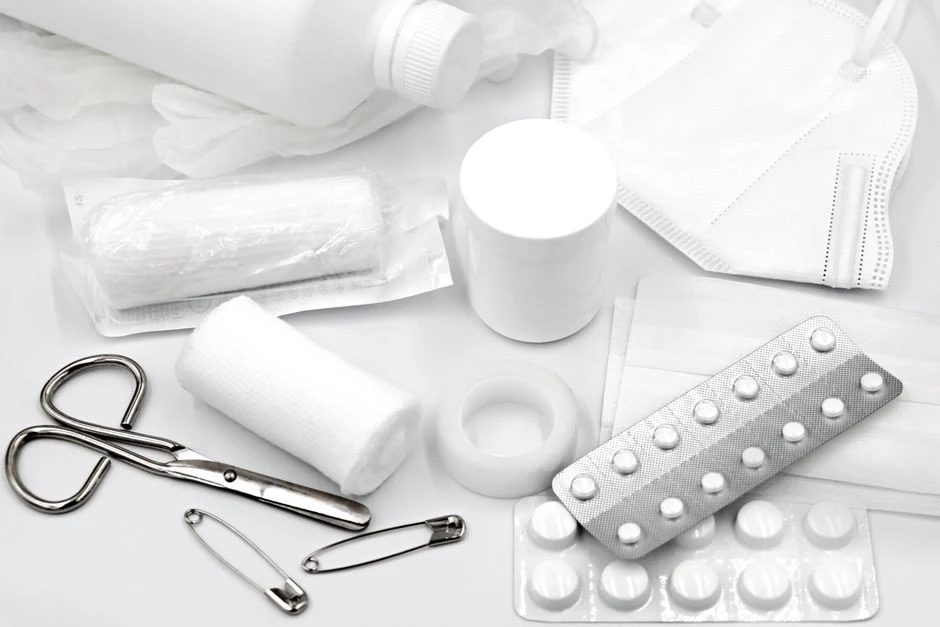 Bandage rolls, scissors, safety pins and blister packs on a white table