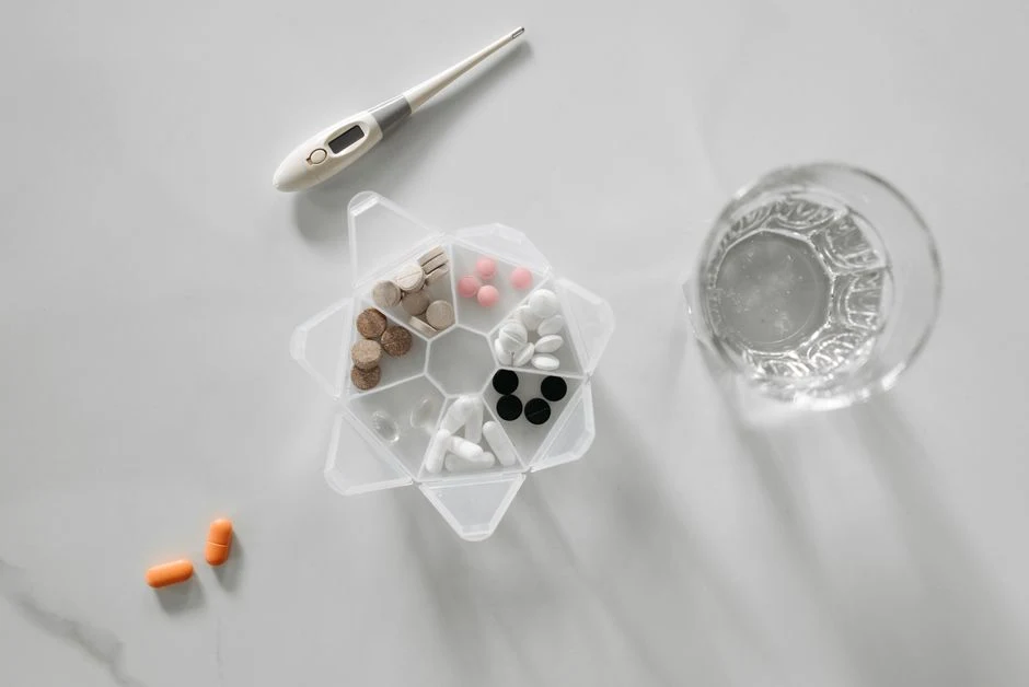 Pill organiser with tablets next to a glass of water on a marble table