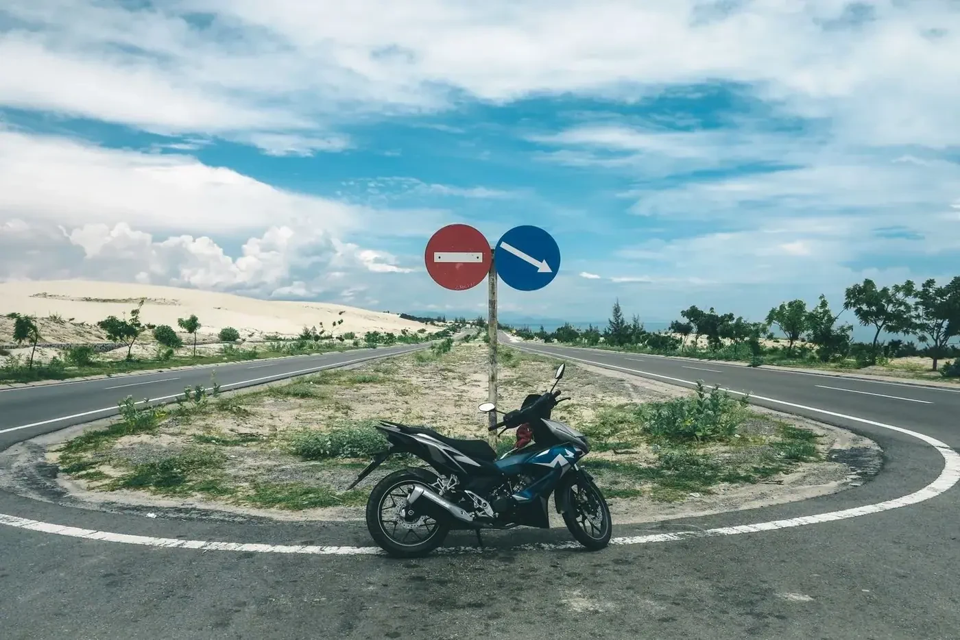 Motorbike parked at a rural road junction near sand dunes and road signs