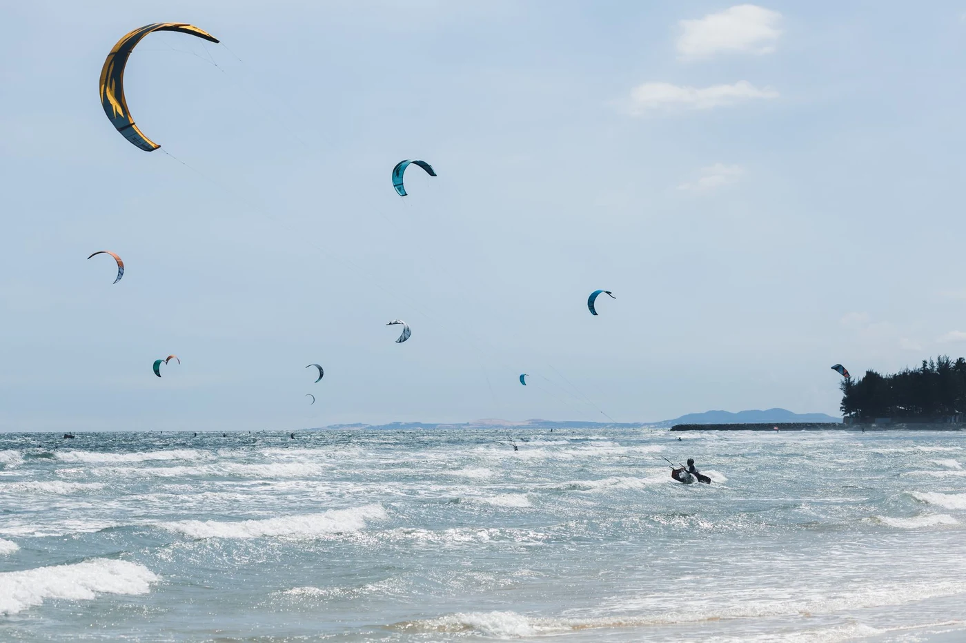 A kiteboarder rides waves near Mui Ne’s tree-lined coast