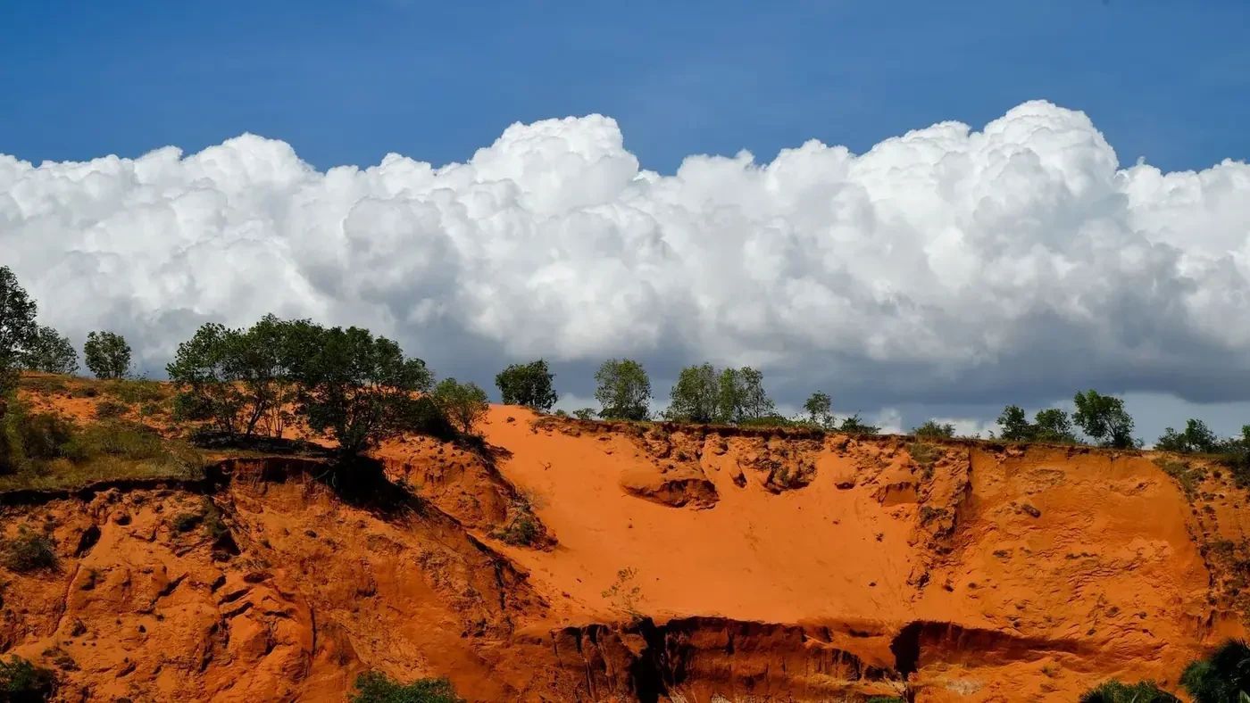 Reddish sand dunes carved into cliffs under a cloudy blue sky