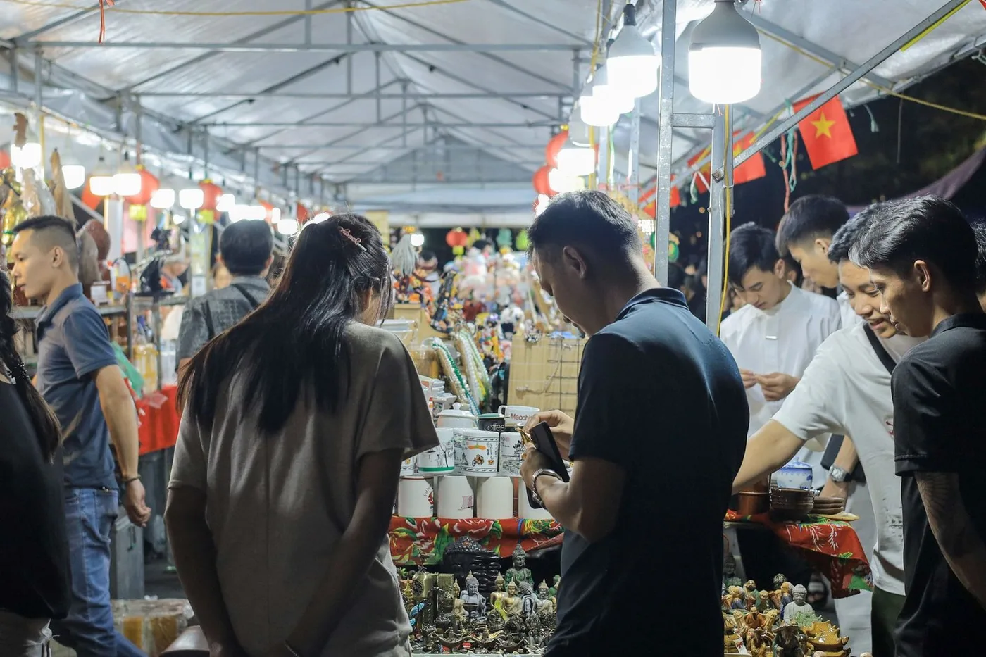 Shoppers browsing souvenir stalls at a night market under bright lamps