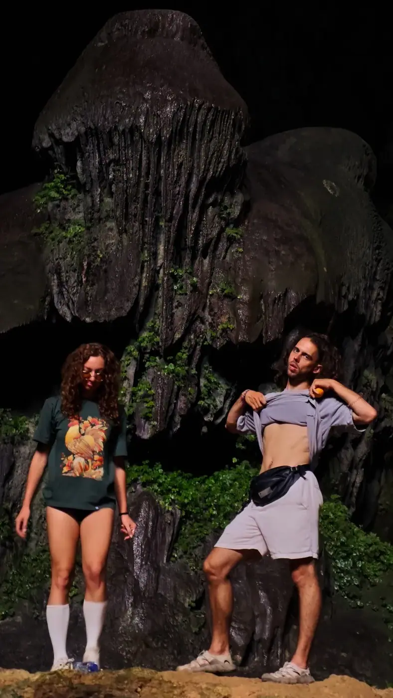 Two travelers exploring a dark limestone cave in Ninh Binh