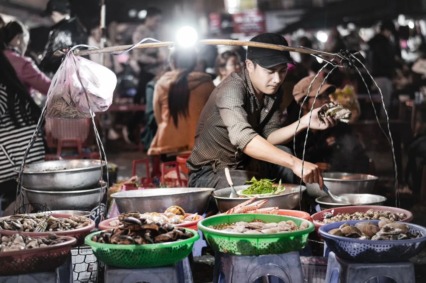 Vendor with baskets of shellfish at a night market stall