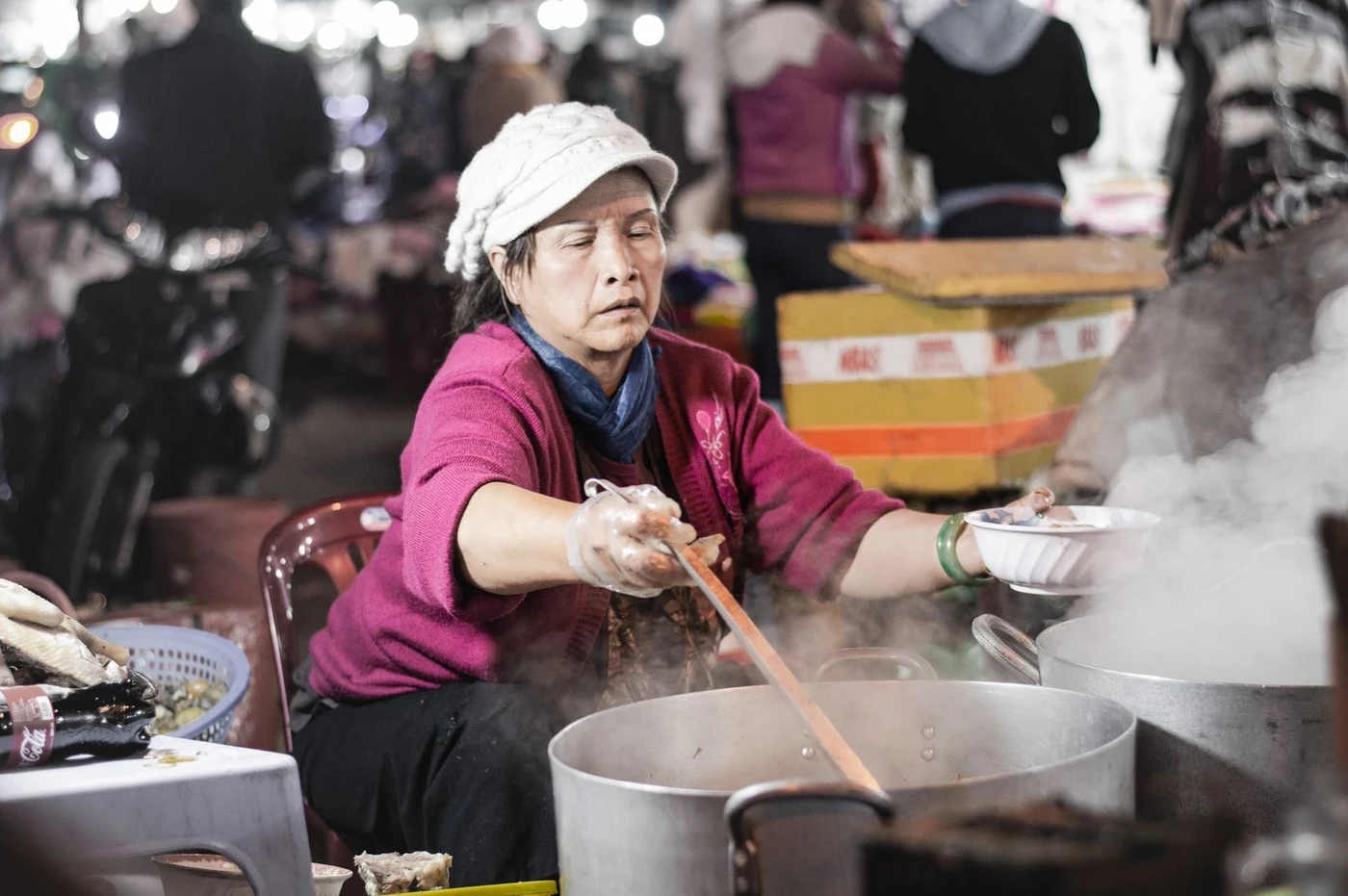 Woman ladling soup from a steaming pot at a market stall