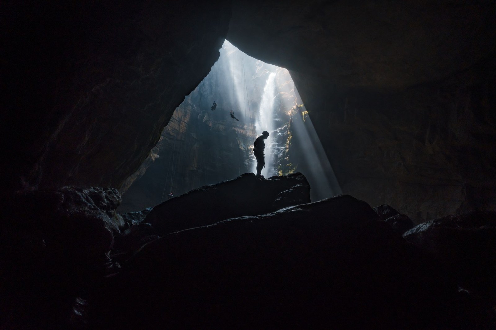 A caver rappelling down a shaft of light inside a limestone cave