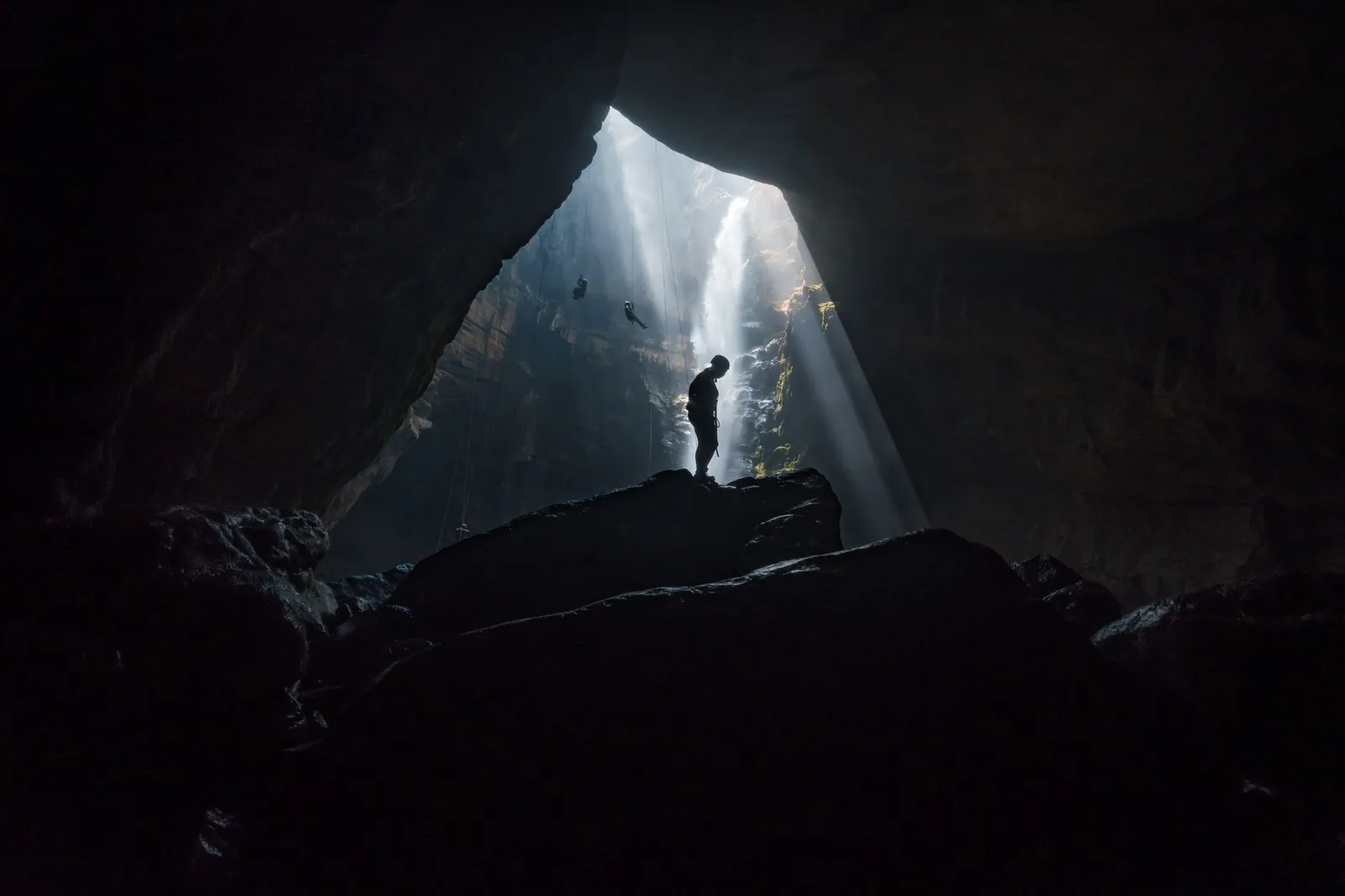 A caver rappelling down a shaft of light inside a limestone cave