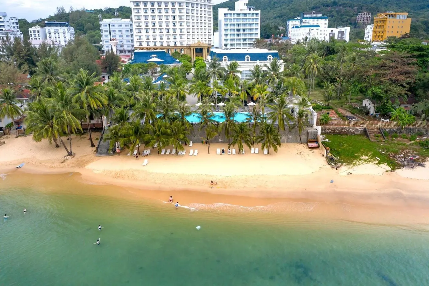 Aerial view of a beachfront resort with a pool and sandy shore