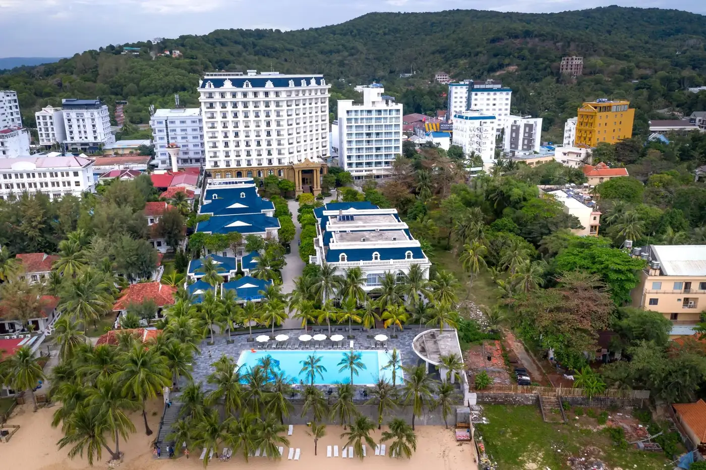 Aerial view of a beach resort with pool and palms among hotel buildings