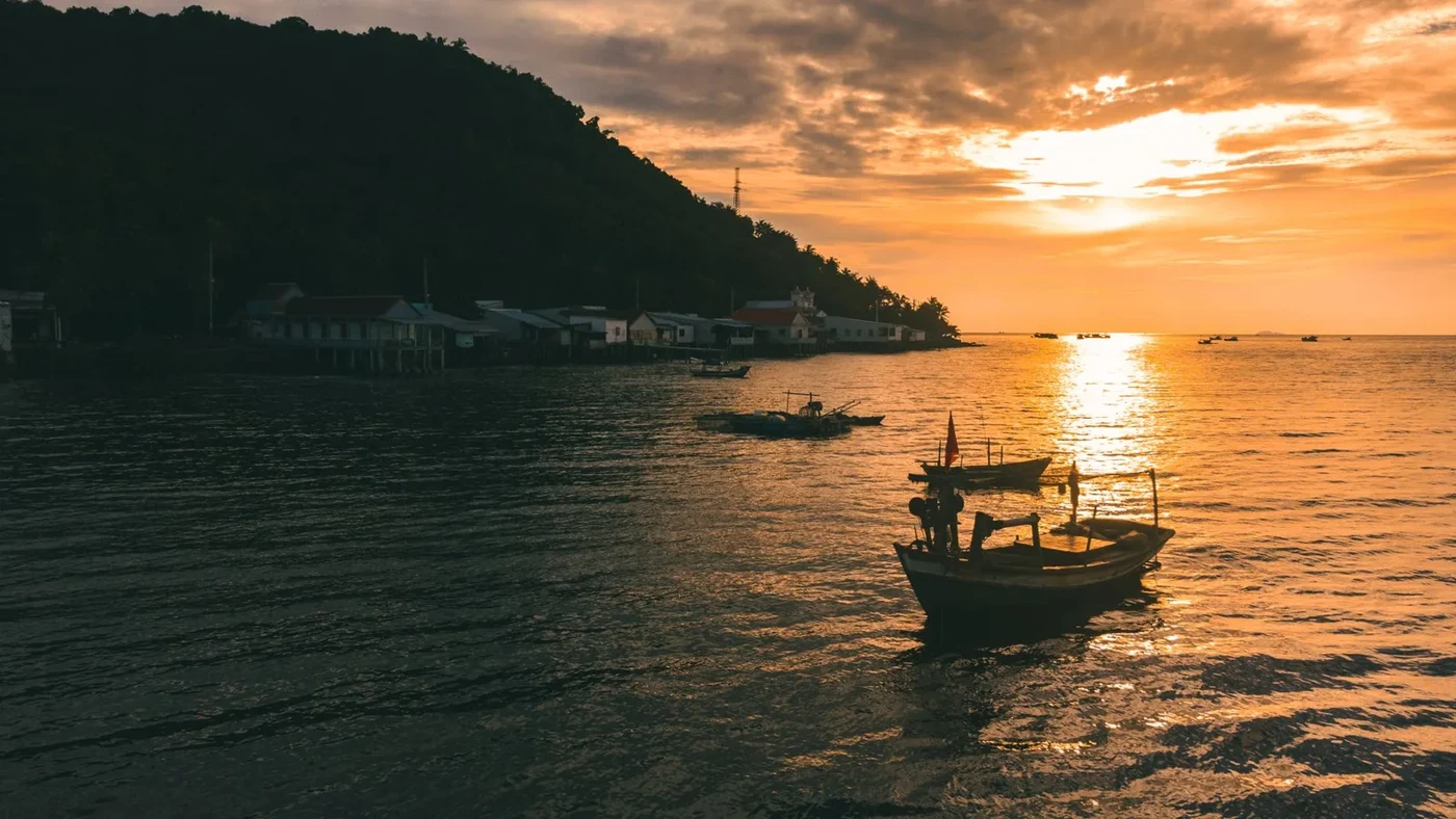 Fishing boats on calm water at golden sunset near a hillside village