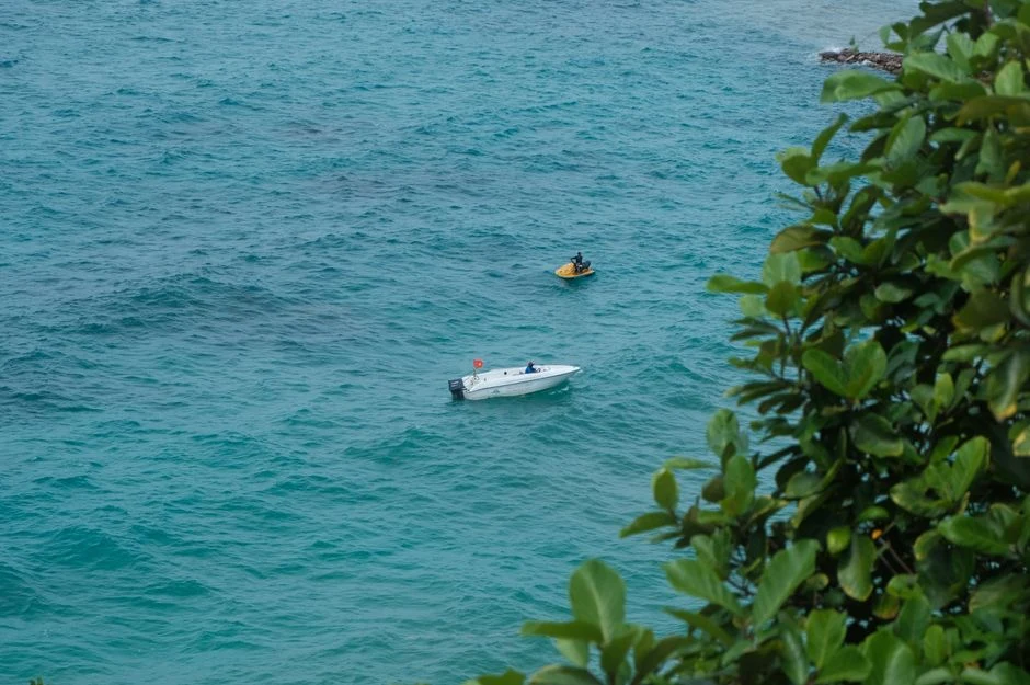 Small speedboat and a jet ski on turquoise water near a green shore