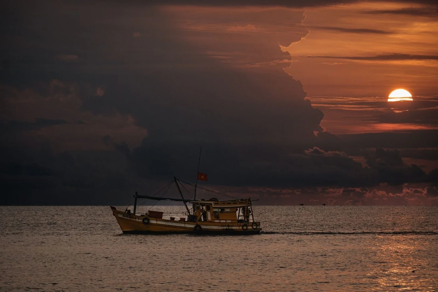Fishing boat with a Vietnamese flag crossing the sea at sunset
