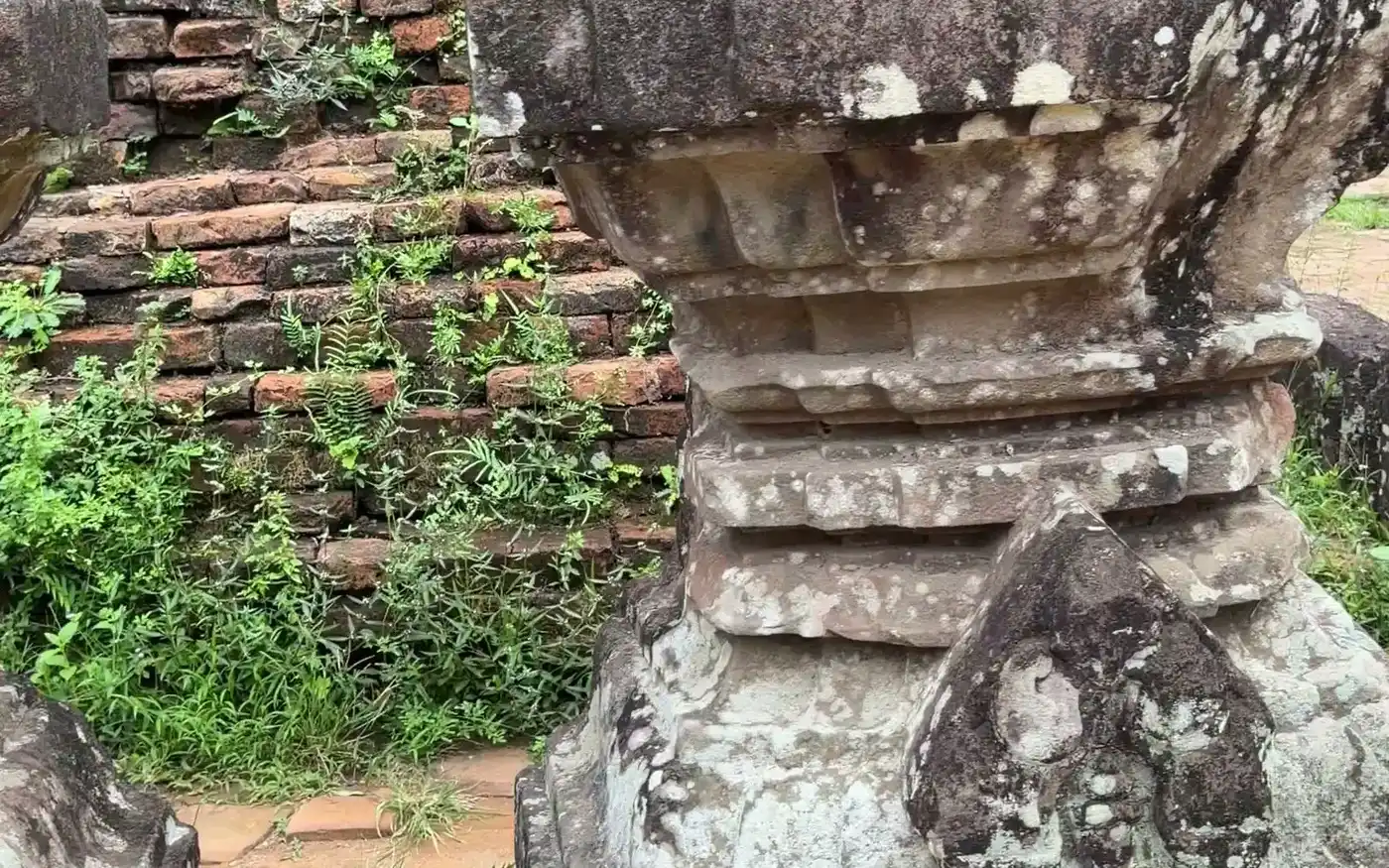 Carved stone pedestal standing against an old brick wall at a Cham temple