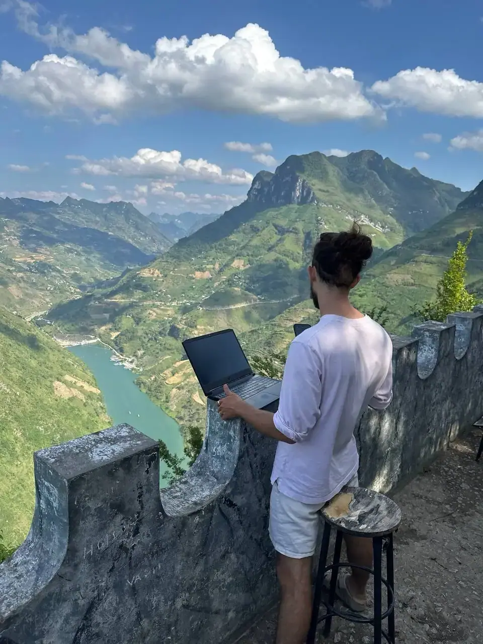 Traveler working on a laptop at a viewpoint above the Nho Que River canyon
