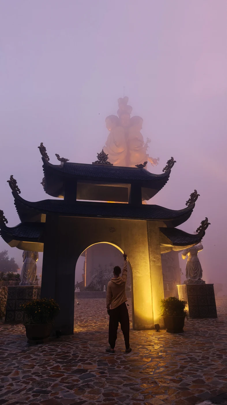 A traveler at the lit gate of a pagoda in the fog on a mountain pass